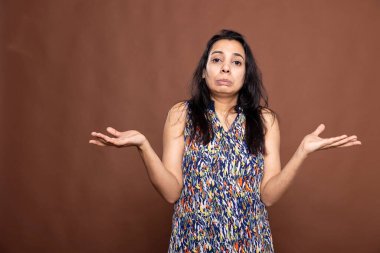 Kafası karışmış dudakları büzüşmüş, omuz silkmiş, belirsizlik ve cehaleti ifade eden Hintli kadın. İzole edilmiş arka planda duran ve güvensiz görünen güzel bir kadın..