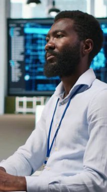 Dikey bilgisayar bilimcisi yapay zekayı kullanarak performansı ve tahminleri optimize ediyor. Ofis eğitim makinesinde çalışan Afrikalı Amerikalı işçi bilgisayar, kamera A kullanarak modeller öğreniyor.