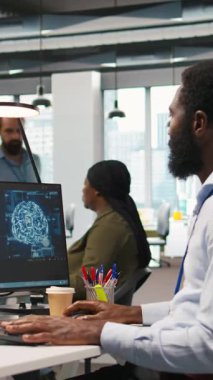 Dikey bilgisayar bilimcisi yapay zekayı kullanarak performansı ve tahminleri optimize ediyor. Ofis eğitim makinesinde çalışan Afrikalı Amerikalı işçi bilgisayar, kamera A kullanarak modeller öğreniyor.