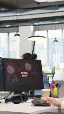 Dikey video Genç tecrübesiz geliştirici kritik hata uyarısını düzeltmeye çalışıyor. Bilgisayar ekranındaki intörn sorun çıkarma hatası bildirimi iş akışını kesiyor, kamera A