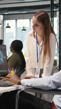 Dikey video mühendisi ve belden aşağısı felçli iş arkadaşı ofiste beyin fırtınası yapıyor, yapay zeka ölçümlerini gözden geçiriyorlar. Tekerlekli sandalyedeki küçük dev ve meslektaşı PC kullanarak sinirsel ağları ayarlıyorlar.