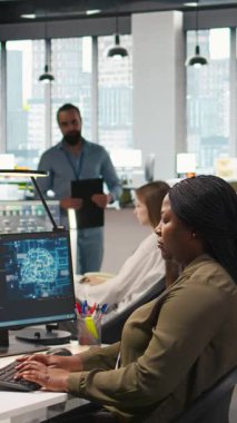 Başlangıç ofisindeki dikey bilgisayar bilimcisi yapay zeka sistem ölçümlerini gözden geçiriyor, performans gösterge panellerini izliyor. Afrika kökenli Amerikalı bir kadın, bilgisayar ve kamera A 'daki araçları kullanarak sinirsel ağları ayarlıyor.