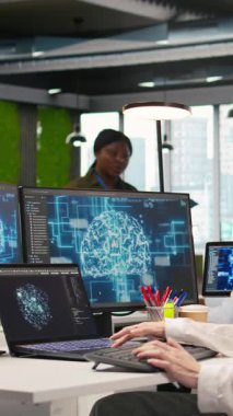 Yüksek teknoloji firma ofisindeki dikey video bilişim uzmanı yapay zeka modelleri geliştirmek için sinirsel ağlar kullanır. Kadın mühendis, aygıtlar üzerinden görevleri çalıştırmak, ekranlardaki ilerlemeyi izlemek için yapay zeka kullanır