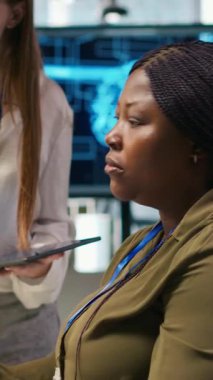 Dikey Video Yöneticisi, genç teknisyene yapay zeka kullanarak yazılımı nasıl geliştireceğini ve nasıl optimize edeceğini öğretiyor. Takım lideri, başkanlık koltuğunda stajyere suni zekanın darboğazı nasıl çözeceği konusunda rehberlik ediyor.