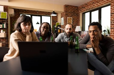 Dört farklı yetişkin şüpheli film izlerken dizüstü bilgisayar ekranına şaşkınlıkla bakıyor. Masada yeşil bira şişeleri olan grup arkadaşları rahat bir dairede takılmayı öneriyorlar..