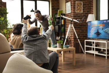 Çok ırklı arkadaşlar, kapalı mekanda eğlenirken video oyunu kazanıp tezahürat yapıyorlar. Atıştırmalık ve içeceklerle dolu genç yetişkinler, tuğla duvarda oyun oynamanın keyfini çıkarıyorlar..