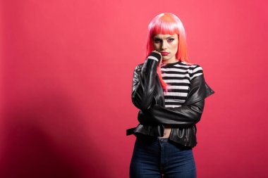 Çizgili bluz ve deri ceketli güzel manken suratını sıkarak somurtuyor. Pembe peruklu güzel beyaz kadın ayakta kameraya somurtkan bir ifadeyle bakıyor..