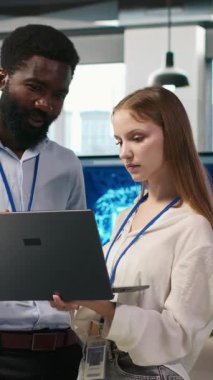 Dikey video Junior Dev ve ofisteki meslektaşı yapay zeka ölçümlerini gözden geçiriyorlar, performans göstergelerini izliyorlar. Teknoloji şirketi programcısı ve genç bayan mühendis sinirsel ağları ayarlıyorlar, kamera A