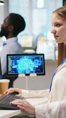 Yüksek teknoloji firma ofisindeki dikey video bilişim uzmanı yapay zeka modelleri geliştirmek için sinirsel ağlar kullanır. Kadın mühendis, aygıtlar üzerinden görevleri çalıştırmak, ekranlardaki ilerlemeyi izlemek için yapay zeka kullanır