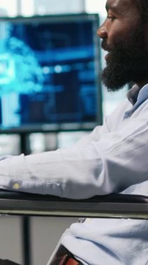 Dikey video mühendisi ve belden aşağısı felçli iş arkadaşı ofiste beyin fırtınası yapıyor, yapay zeka ölçümlerini gözden geçiriyorlar. Tekerlekli sandalyedeki küçük dev ve meslektaşı PC kullanarak sinirsel ağları ayarlıyorlar.