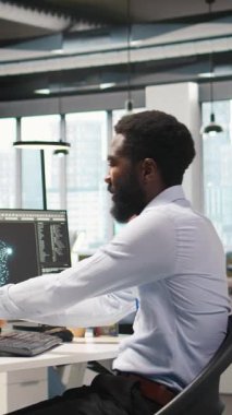 Dikey video yazılım geliştiricisi üretken yapay zeka makinesini test ediyor algoritmaları öğreniyor ve iş yerinde müzik dinliyor. Kulaklık takan Afrikalı Amerikalı adam yapay zeka ile üretkenliği artırıyor.