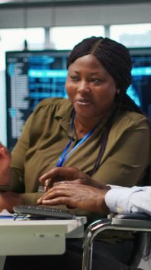 Tekerlekli sandalyedeki dikey video ofis mühendisi iş arkadaşıyla konuşuyor, yapay zeka modelleri geliştiriyor. Belden aşağısı felçli bilişim uzmanı ve yapay zeka simülasyonları yapan iş arkadaşı.