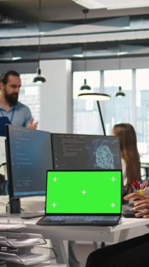 Ofisteki iş arkadaşlarının yanında dikey video teknisyeni, yeşil ekran dizüstü bilgisayar kullanarak yazılım uygulamaları geliştiriyor, yapay zeka otomasyonunu entegre ediyor. IT uzmanı model defter ve kamera ile hata ayıklama uygulamaları yapıyor