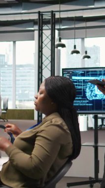 Ofis arkadaşlarının yanında dikey video teknisyeni yazılım uygulamaları geliştiriyor, yapay zeka otomasyonunu entegre ediyor. İş yerindeki geliştiricilerin yanındaki Afrikalı Amerikalı adam hata ayıklıyor