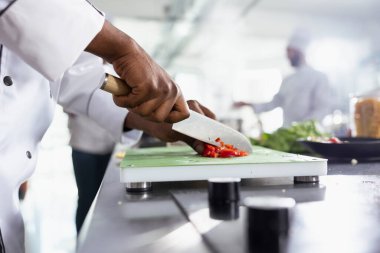 Mutfak işçisi kırmızı dolma biber kesiyor ve gurme yemeği için taze malzemeler hazırlıyor. Çalışma alanı mutfak aletleri ve taze ürünlerle dolu, gastronomi için çiğ sebzeler. Kapat..