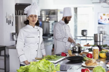 Kalabalık bir restoran mutfağında, üniformalı şef mutfak tezgahında paslanmaz çelik aletler kullanarak lezzetli yemekler pişiriyor. Yemek hazırlama tekniklerinde ustalaşmak.