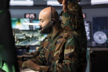 Askeri sevkiyat memuru monitörlerdeki izleme iletimine bakıyor. Kulaklık mikrofonuyla askerlere bilgi aktarıyor. Askeri ajan keşif bilgilerini iletiyor.