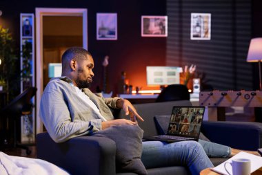 Kendine güvenen erkek konuşmacı web sitesindeki bir video konferans toplantısında iş arkadaşlarını selamlıyor, rahat çatı katında çevrimiçi uzaktan iletişimin faydalarından faydalanıyor. Siyah adam sanal tartışma sunuyor..