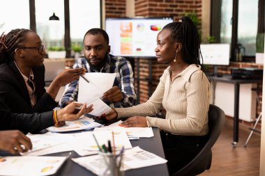 Afrika kökenli Amerikalı meslektaşlar konferans masasının etrafında toplanarak mali raporları tartıştılar ve analiz ettiler. Belgeleri olan erkek ve kadın çalışanlar değerlendirme toplantısında pazarlama planlarını gözden geçiriyorlar..