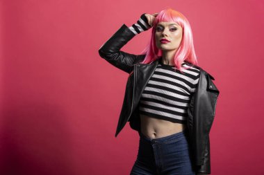 Pembe arka planda kalın, modaya uygun kıyafetler giyen kendine güvenen bir kadın model. Çekici bir kadın dik duruyor. Odaklanmış gözleri ve sıkı vücut duruşuyla kameraya bakıyor..