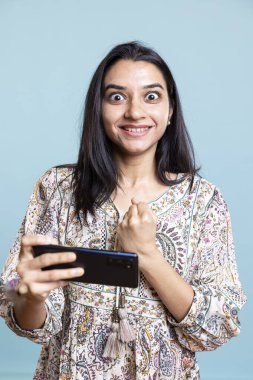 Mobil video oyunlarını kazanan mutlu kız mavi arka plana karşı galibiyeti ve başarıyı kutluyor. Genç bir kadın oyun yarışmasını sevdiği için heyecanlı..