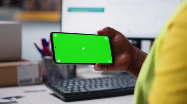 Hi vis yeleğindeki depo işçisi telefonda yazılım yönetimi, ambalaj sistemleri ve envanter yönetim araçları için kroma anahtar görüntüsü kullanıyor. E-ticaret lojistiği. Kamera B.