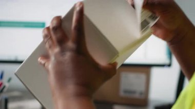 Karton kutulara nakliye etiketleri yapıştıran kadın lojistik işçisi, etiketlerde barkod izleme bilgileri olan bir depoda yelek giyen kadın. Sipariş tamamlama ve paket takibi. Kamera B.