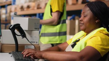 Engelli Afrikalı Amerikalı işçi, dağıtım merkezindeki sipariş paketini izlemek ve yazılım bilgilerini takip etmek için havayolu fatura numaralarını kullanıyor. Sevkiyat operasyonlarını yönetiyorum. Kamera B.