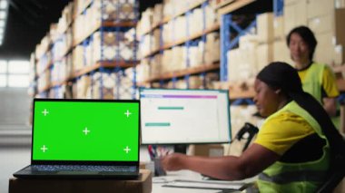 Personel veri girişi, envanter izleme motifleri ve görsel veya barkod yazıcı arayüzleri için depo odasındaki krom anahtar monitörünü gözden geçirir. Lojistik işçisi kargoyu ön planda paketler. Kamera A.