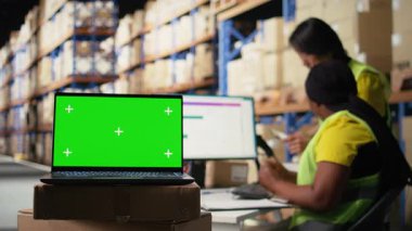 Lojistik çalışanı bilgisayarda izole edilmiş modellerin yanında paketler düzenliyor, sipariş izleme araçları yerleştiriyor ve etiketleme sistemleri yerleştiriyor. Personel üyesi, iş envanterini analiz ediyor. Kamera A.