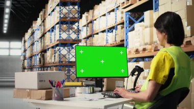 Personel veri girişi, envanter izleme motifleri ve görsel veya barkod yazıcı arayüzleri için depo odasındaki krom anahtar monitörünü gözden geçirir. Lojistik işçisi kargoyu ön planda paketler. Kamera A.