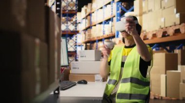 Asyalı adam sanal gerçeklik kulaklığı kullanıyor ve endüstriyel depolama raflarının yanında takip yazılımı kullanıyor, emirleri işliyor. Paketlerin izleme bilgilerini güncellemek için VR cihazı, yapay zeka. Kamera A.