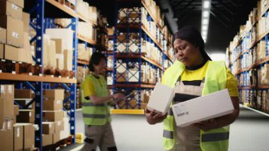 Afro-Amerikan işçilerinin portresi, kargo sevkiyatından önce paketlenmiş kutuları ve etiketleri kontrol ederek, perakende satış için siparişin yerine getirilmesini garanti altına alıyor. Lojistik merkezi aktivitesi. Kamera A.
