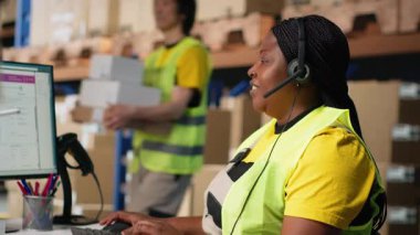 Siyahi kadın müşteri destek memuru müşterilerle sevkiyat detayları hakkında konuşuyor, yardım hattında yanlış adres karışıklığına yardım ediyor. Kadın siparişi çözer, havayolu faturalarını onaylar. Kamera B.