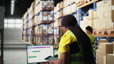 Afrika kökenli Amerikalı işçiler e-ticaret kargo siparişlerini depo ortamında işliyor, çelik yelek giyiyor ve kusursuz bir dağıtım sağlıyor. Büyük raflarda depolanmış karton kutular. Kamera A.