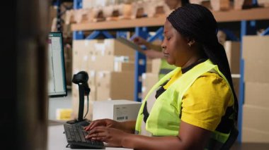 Bilgisayarda sevkiyat detaylarını yazan Afrikalı Amerikalı kadın işçiler, müşteriler için paket izleme yazılımlarını güncelliyorlar. Perakende depo tesisinde sipariş yerine getirilmesi. Kamera B.