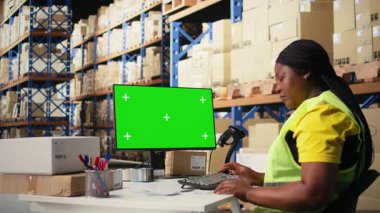 Siyah kadın işçiler yeşil ekran, depo otomasyon araçları ve envanter kontrol panellerinin yanında sipariş veriyor. Depolama raflarıyla birlikte e-ticaret emri işlemleri. Kamera A.