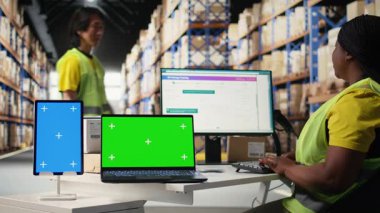 Yeşil ekran monitörünün yanındaki depoda çalışan çok ırklı bir ekip. Nakliye etiketlerini, barkod tarayıcı verilerini ya da endüstriyel depodaki envanter izleme sistemlerini yönetmek. Kamera A.
