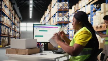 Siyah depo çalışanı etiketleme ve paketleme işlerini yönetir, basılı hava yolu faturalarını paketlere takip numaraları etiketleri ile uygular. Depoda yüksek çözünürlüklü kadın var. Kamera A.