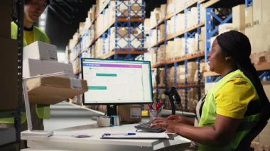 Bir dağıtım merkezinde ambalaj işlemleri sonrasında, gelecekte sipariş takibi için barkod gönderme etiketlerini kaydetmek için tarayıcı kullanan siyah bir çalışan, awb etiketlerini tarıyor. Depo odası. Kamera A.