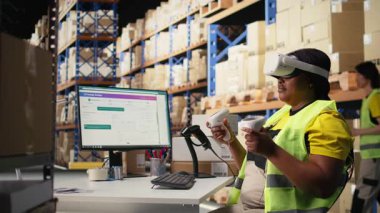 Afro-Amerikalı bir kadın siparişleri işlemek ve paket sevkiyatını yönetmek için sanal gerçeklik sisteminde çalışıyor, ücretsiz envanter kontrolü yapıyor. Sanal gerçeklik hızlı teslimatı garanti eder. Kamera A.