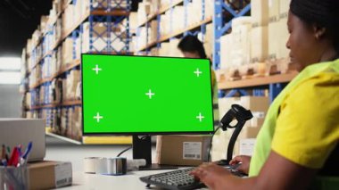 Lojistik çalışanı bilgisayarda izole edilmiş modellerin yanında paketler düzenliyor, sipariş izleme araçları yerleştiriyor ve etiketleme sistemleri yerleştiriyor. Personel üyesi, iş envanterini analiz ediyor. Kamera A.