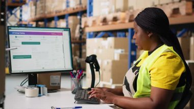 Bir dağıtım merkezinde ambalaj işlemleri sonrasında, gelecekte sipariş takibi için barkod gönderme etiketlerini kaydetmek için tarayıcı kullanan siyah bir çalışan, awb etiketlerini tarıyor. Depo odası. Kamera B.