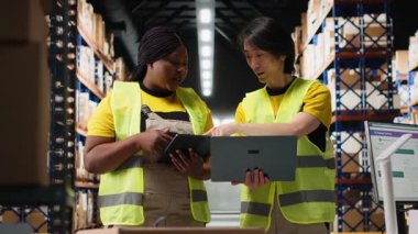 Endüstriyel depodan gelen raflı kargo sevkiyatını takip eden çeşitli işçiler, tabletteki paket durumları için takip yazılımlarıyla ilgileniyorlar. Çelik yelek personeli. Kamera B.