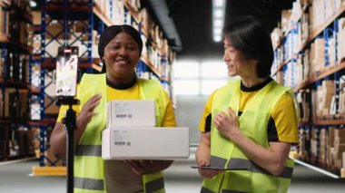 Afro-Amerikan ve Asyalı ekipler kargo mallarını canlı yayında sunuyorlar. Rafların yakınındaki endüstriyel depoda bir video kaydı yapıyorlar. Büyük iş reklamları için içerik. Kamera B.