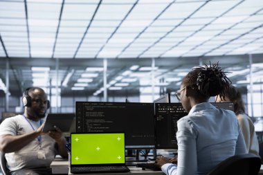 BT destek uzmanlarının önünde veri merkezinde sunucu satırlarını denetleyen yeşil ekran dizüstü bilgisayar. Çalışanlar süper bilgisayarları denetlemek için model defter aygıtı kullanırlar