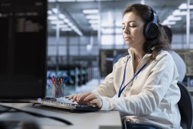 Makine öğrenme eğitimi için kullanılan veri merkezinde müzik dinleyen geliştirici. Kulaklık takan bir bilişim uzmanı yapay zeka teknolojisini geliştirmek için kod kullanıyor.