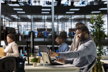 Güvenilir siyah genel müdür ofiste birden fazla iş yapıyor ve bilgisayarındaki idari görevleri çözüyor. Stratejik kararlar alırken belgelerin gözden geçirilmesi ve teslim tarihlerinin tutturulması.