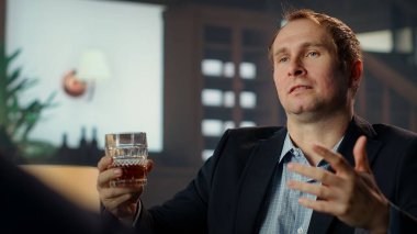 Seçkin bir sosyete üyesi, üst sınıf bir iş birliğinde bir ortakla karışık viski içerek görüşmeler yapıyor. Seçkin üst sınıf beyefendiler servet kazanıyor. Kamera B.