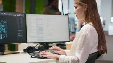 Yapay zeka ile kodlama yapan kadın teknisyen. Başlangıç ofisinde, müzik dinliyor. Kulaklık takan genç bir kadın LLM asistanı önerilerini kod editörü kamera A 'ya entegre ediyor.